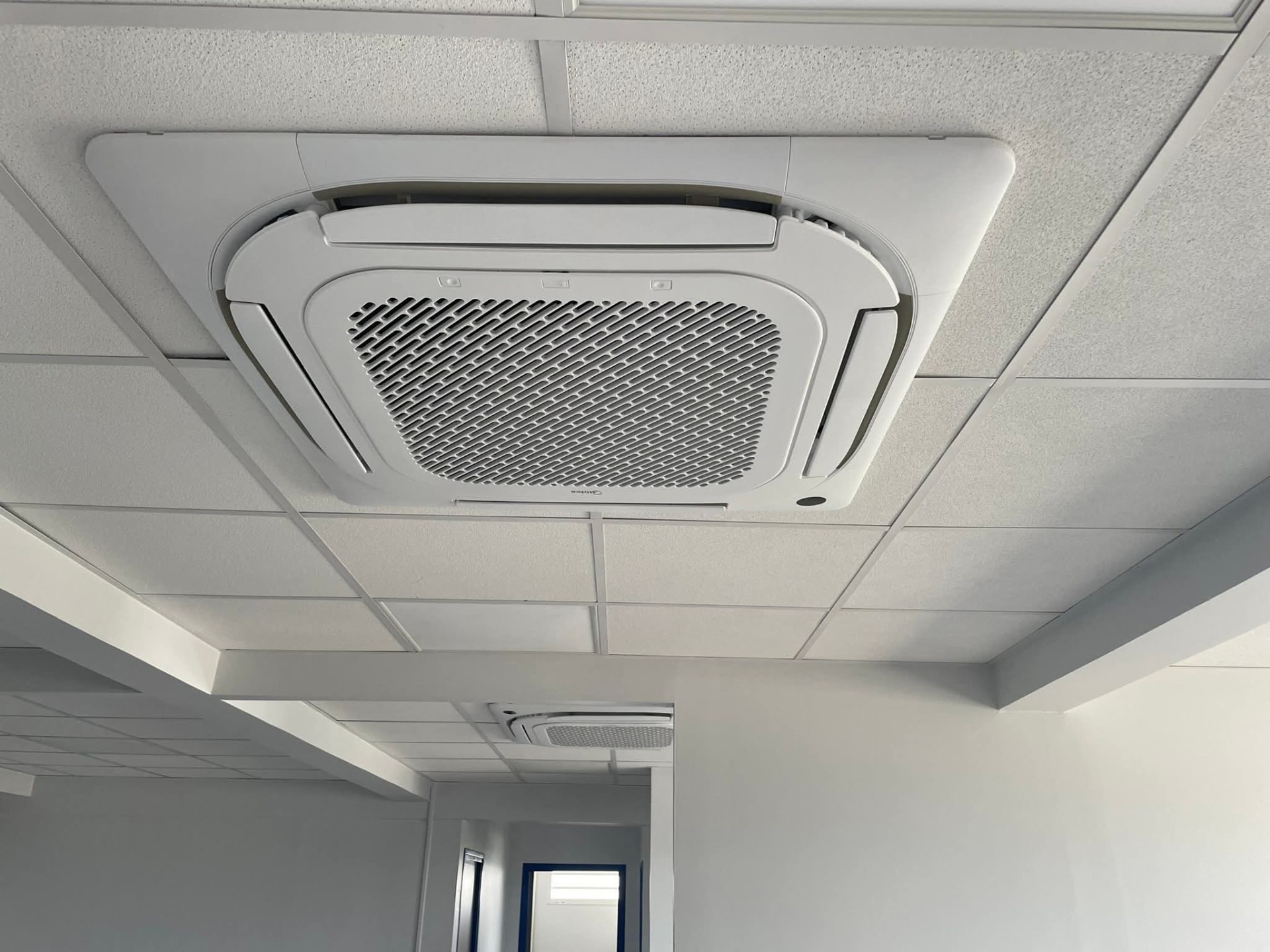 Installation – Lamentin – climatisation Martinique Cassette de plafond Midea encastrée dans un faux-plafond blanc au Lamentin, une seconde cassette visible au fond du couloir pour climatiser tout l'étage – Lamentin, Martinique – LD CLIM 972