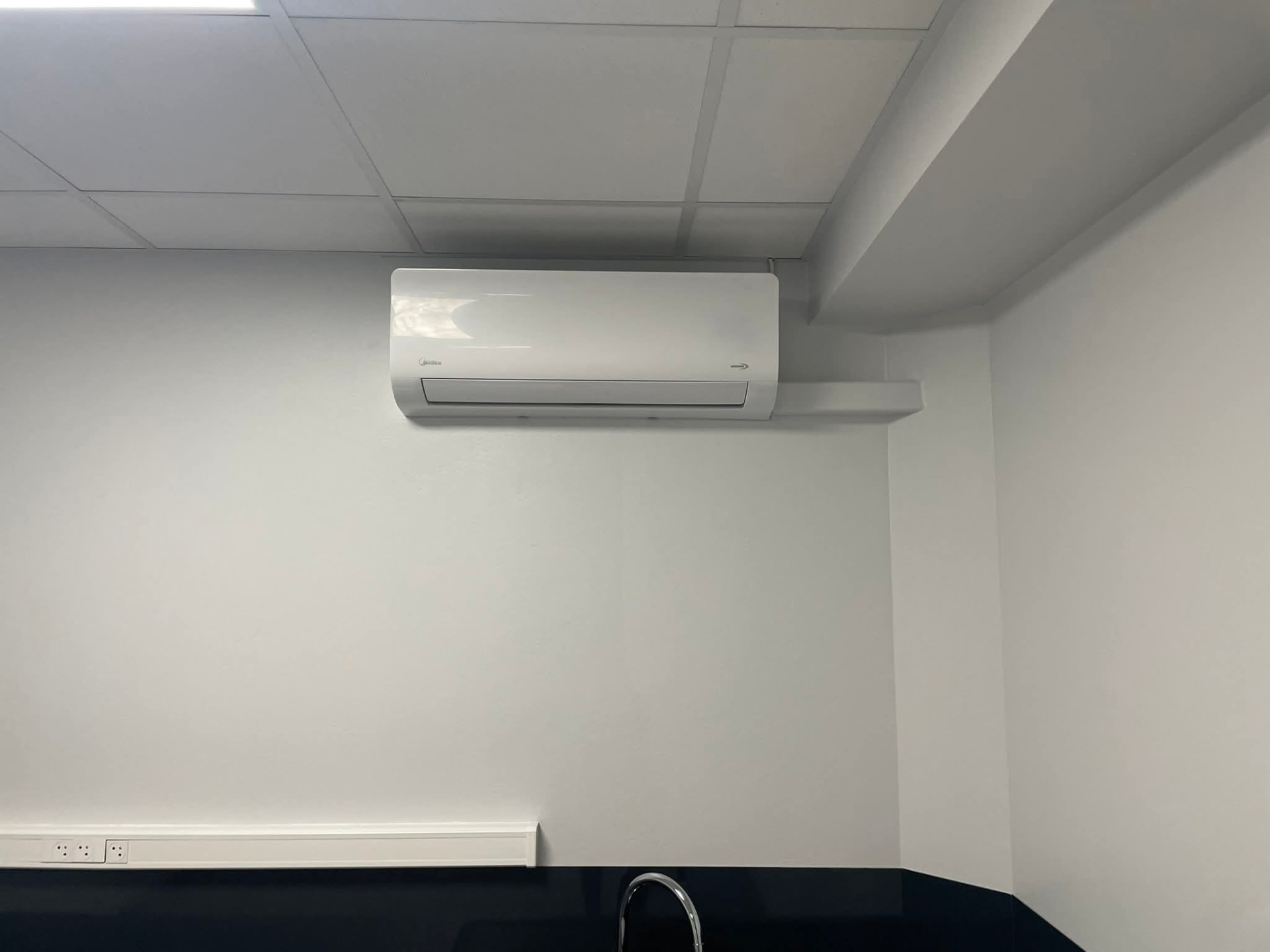 Installation – Lamentin – climatisation Martinique Climatiseur mural Midea installé dans le coin cuisine d'une entreprise au Lamentin, liaisons protégées par une goulotte blanche au-dessus du point d'eau – Lamentin, Martinique – LD CLIM 972