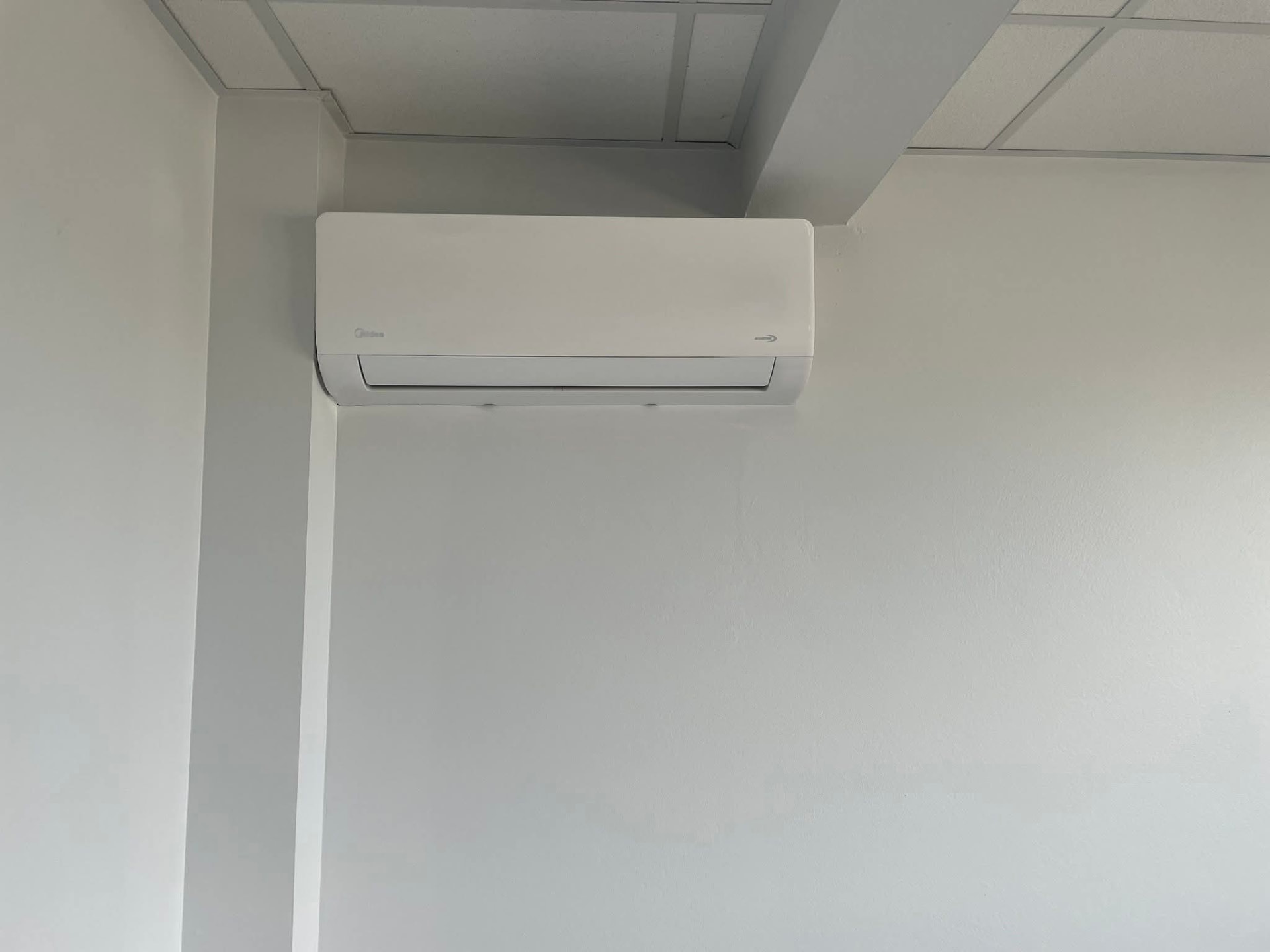 Installation – Lamentin – climatisation Martinique Climatiseur mural Midea fixé en partie haute d'un mur blanc au Lamentin, aligné le long d'un décroché de mur sous le plafond pour une pose discrète – Lamentin, Martinique – LD CLIM 972